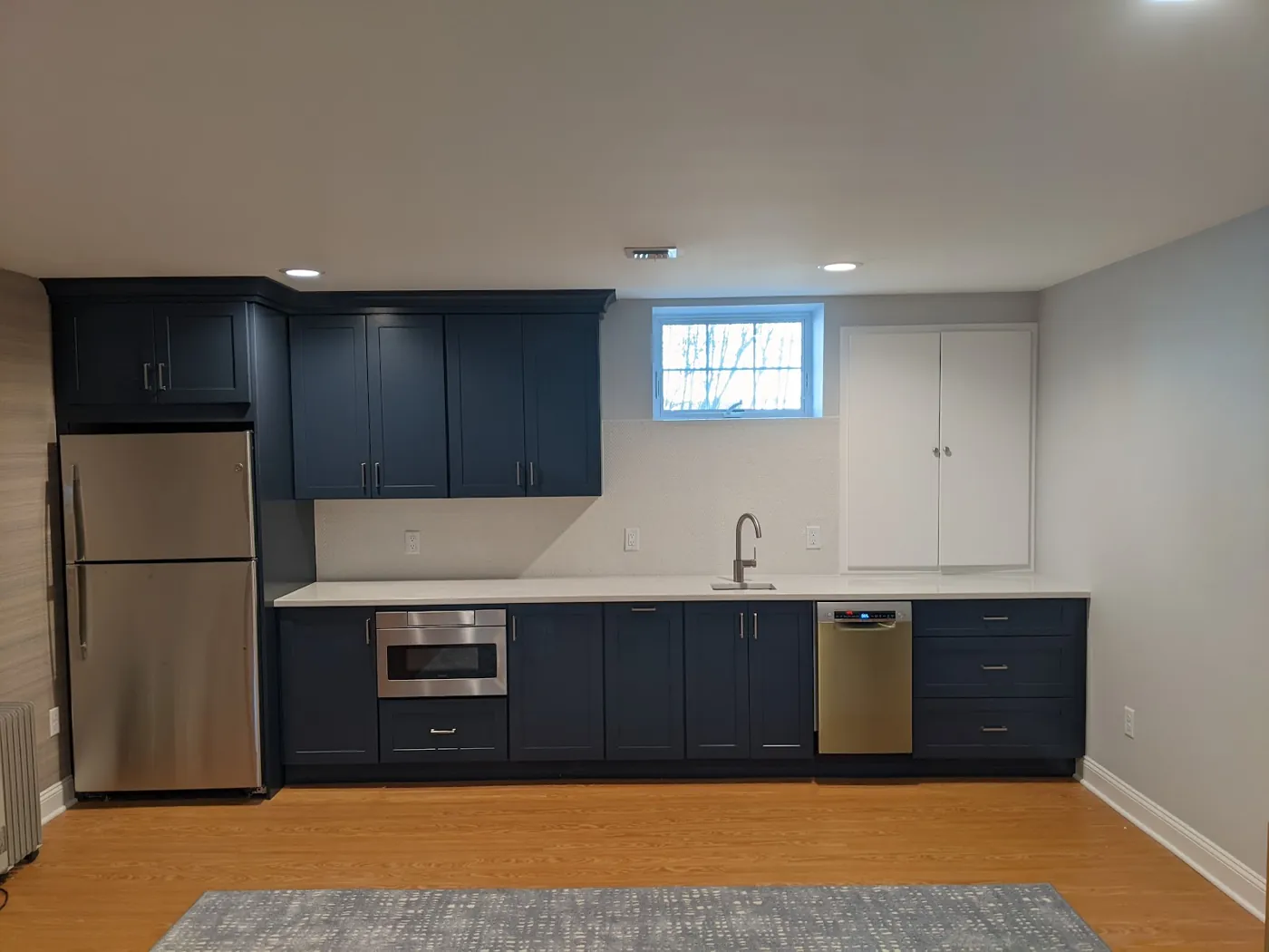 Finished basement in Monmouth County, NJ with a navy kitchenette, quartz counter, and recessed lighting by RSC Contracting