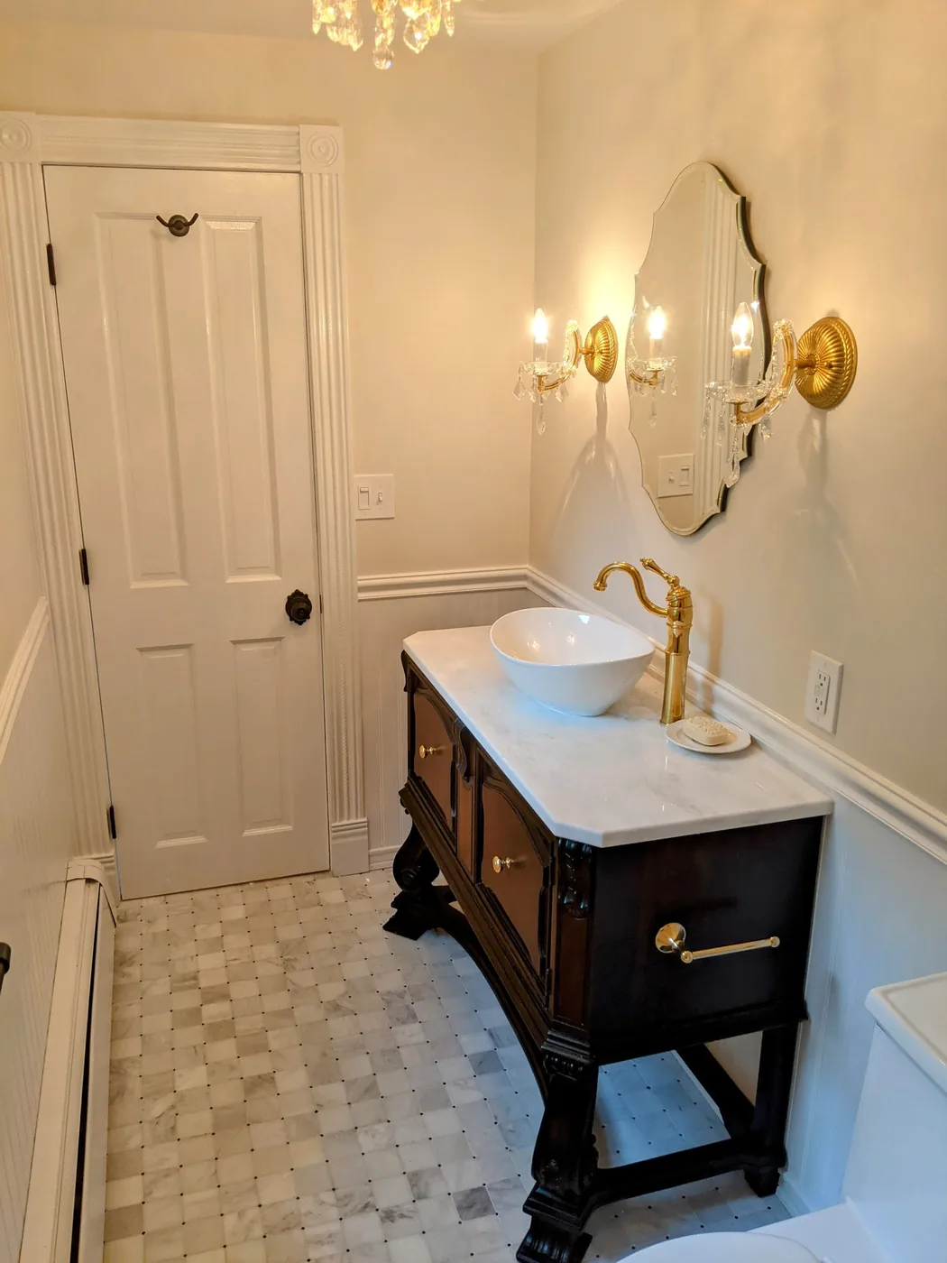 Hall bathroom remodel in Hazlet, NJ with an antique dark wood vanity, a vessel sink, a brass faucet, and a marble basketweave tile floor