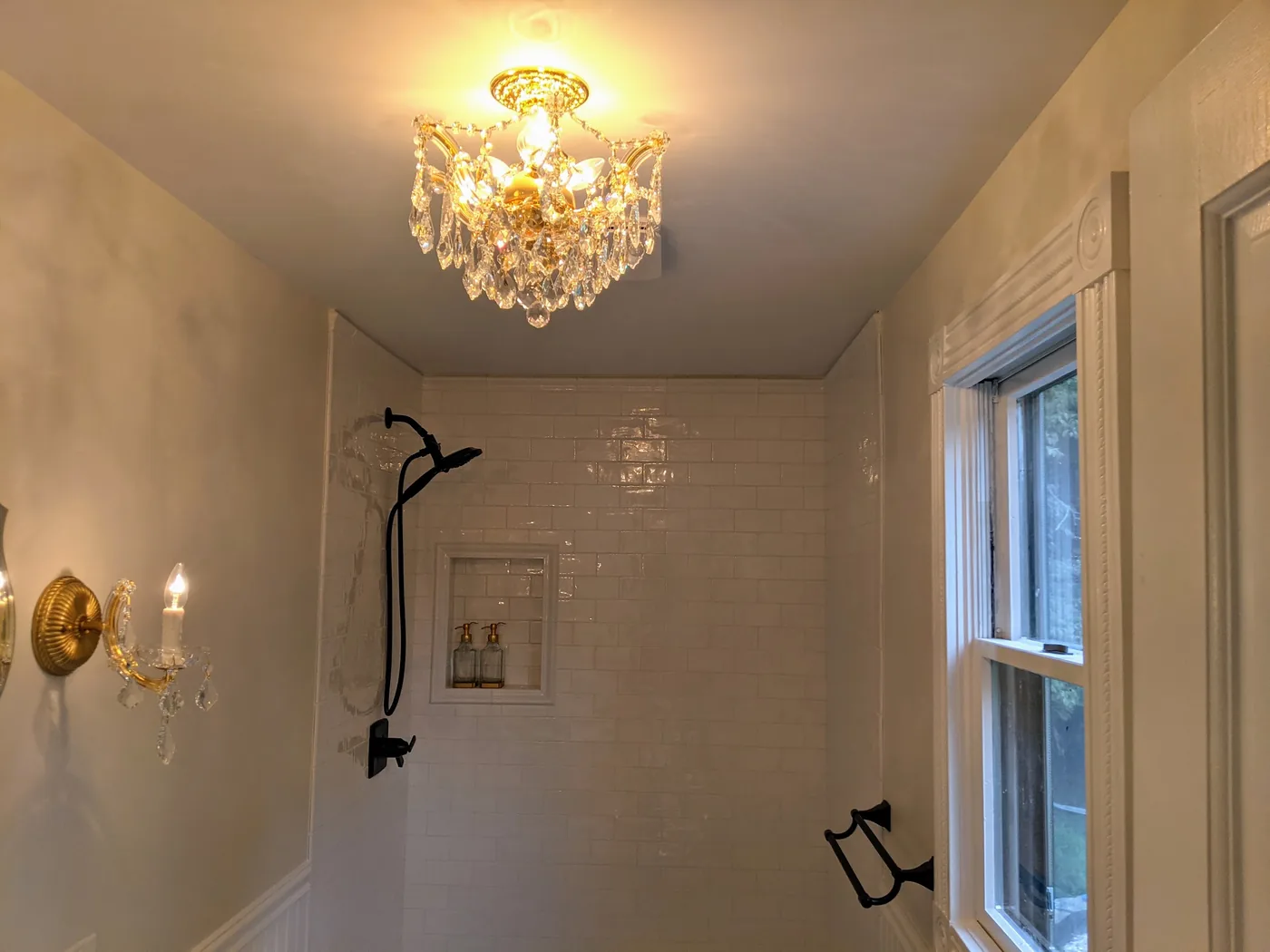 Finished hall bathroom in Hazlet, NJ with a white subway tile shower, a recessed niche, a crystal ceiling fixture, and brass sconces