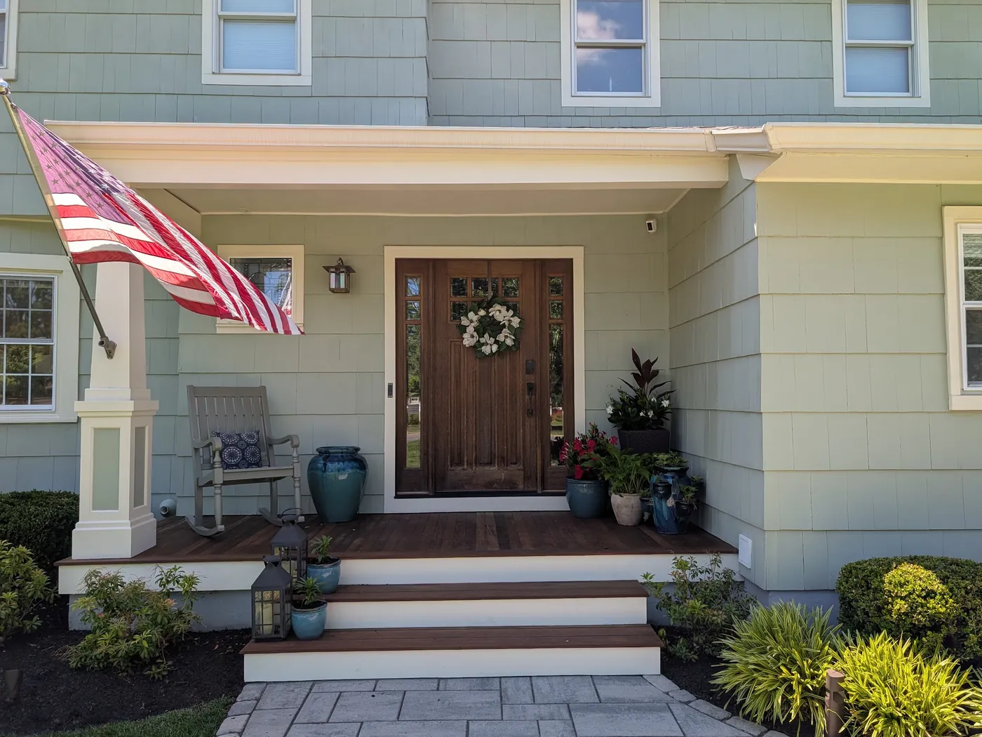 After: a stained craftsman entry door with sidelights under a new covered front porch with white columns, ipe decking, and a paver walk