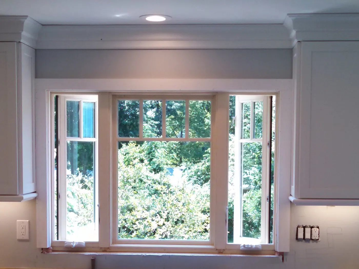 Kitchen window over the sink in Monmouth County, NJ: a fixed center pane flanked by two open casements, set between white cabinets with crown molding