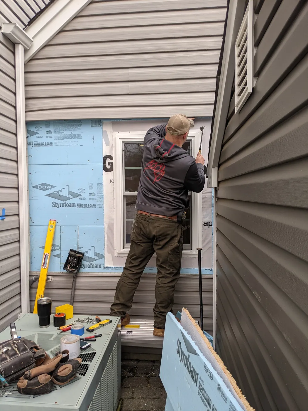 Rob Crotzer setting a replacement window from outside, with the vinyl siding removed around the opening and rigid foam sheathing exposed