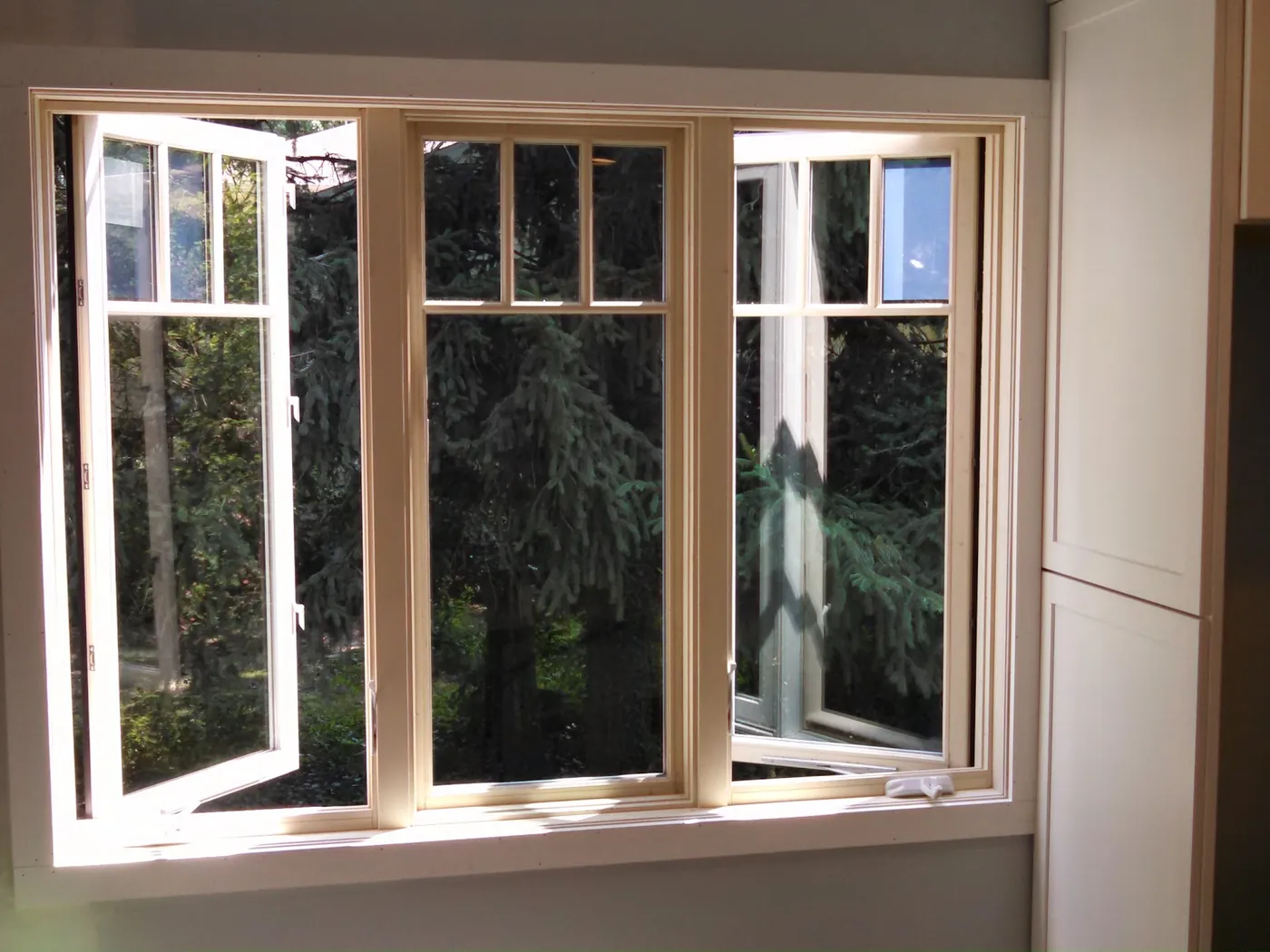Three-unit casement window with a natural wood interior and divided-lite tops, both side casements open, in a Monmouth County, NJ home